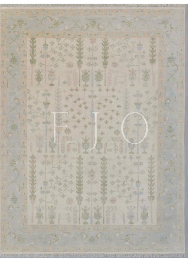 May include: A beige rug with a light blue border and a repeating pattern of stylized plants and flowers. The rug has a subtle, faded look, giving it a vintage feel.