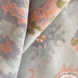 Op de afbeelding: Close-up van een tapijt met een lichtblauwe achtergrond en roze, groene en blauwe patronen. Het tapijt heeft een zacht, getextureerd oppervlak.