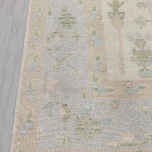 May include: A light blue and pink patterned rug with a fringe border. The rug has a floral design with green leaves and pink flowers.