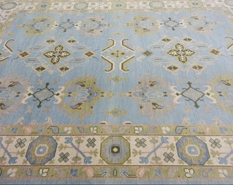 May include: A blue rug with a traditional Persian design. The rug has a light blue background with a green, white, and beige pattern. The rug has a border with a repeating pattern of octagons and squares.