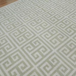 May include: A white rug with a light green geometric pattern. The pattern is a repeating Greek key design.
