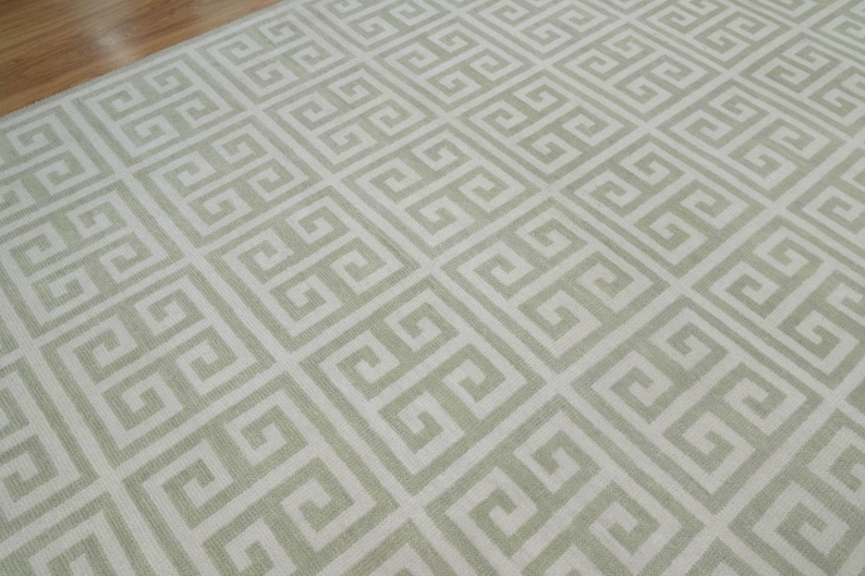 May include: A white rug with a light green geometric pattern. The pattern is a repeating Greek key design.
