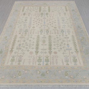 May include: A beige rug with a light blue border and a floral pattern. The rug has a fringe on the edges.