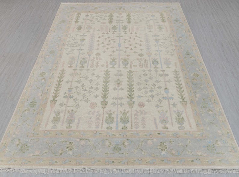 May include: A beige rug with a light blue border and a floral pattern. The rug has a fringe on the edges.