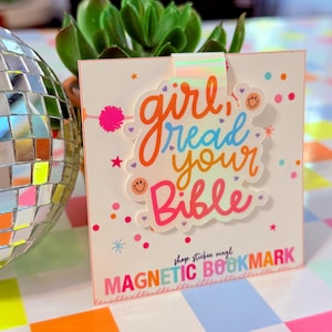 May include: A magnetic bookmark with the text "girl read your Bible" in orange, blue, and pink. The bookmark has a white background with colorful confetti and stars. The words "MAGNETIC BOOKMARK" are at the bottom.
