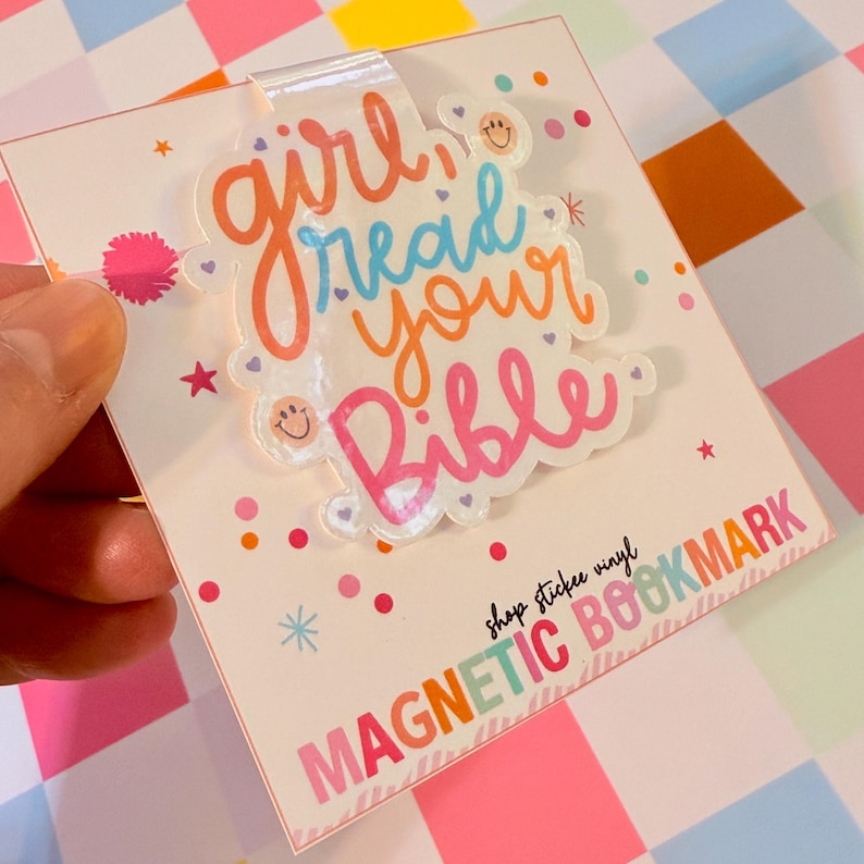 May include: A magnetic bookmark with the text "girl read your Bible" in orange, blue, and pink. The bookmark has a clear plastic overlay and is decorated with small stars and smiley faces. The bottom of the bookmark reads "MAGNETIC BOOKMARK".