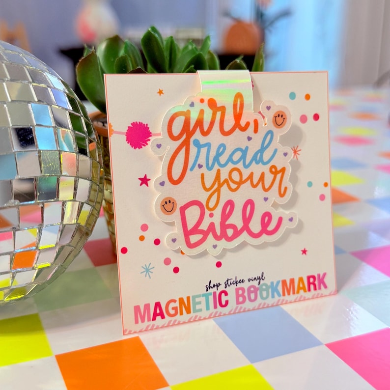May include: A magnetic bookmark with the text "girl read your Bible" in colorful lettering. The bookmark has a white background with pink, orange, and blue accents. The words "MAGNETIC BOOKMARK" are printed at the bottom.