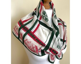 May include: A white silk scarf with green and red stripes and floral designs. The scarf is folded and tied around a mannequin's neck.