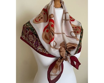 May include: A white silk scarf with a red, green, and gold pattern of stylized faces. The scarf is tied around a mannequin's neck.
