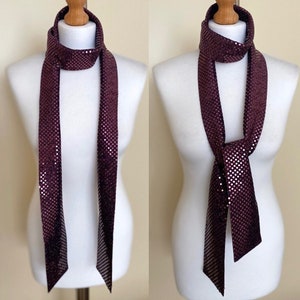 May include: A burgundy sequined scarf with a subtle shimmer. The scarf is shown tied in a simple knot around a mannequin's neck.