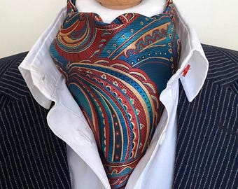 May include: A patterned ascot in shades of teal, red, and gold, worn with a white collared shirt and a pinstripe suit jacket. The ascot features an intricate paisley design.