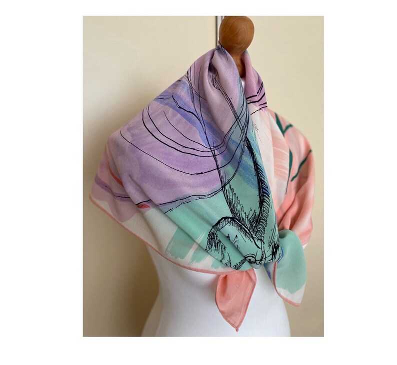 Puede incluir: Una bufanda de seda rosa, verde y morada con un dise&ntilde;o abstracto en blanco y negro. La bufanda est&aacute; atada alrededor del cuello de un maniqu&iacute;.
