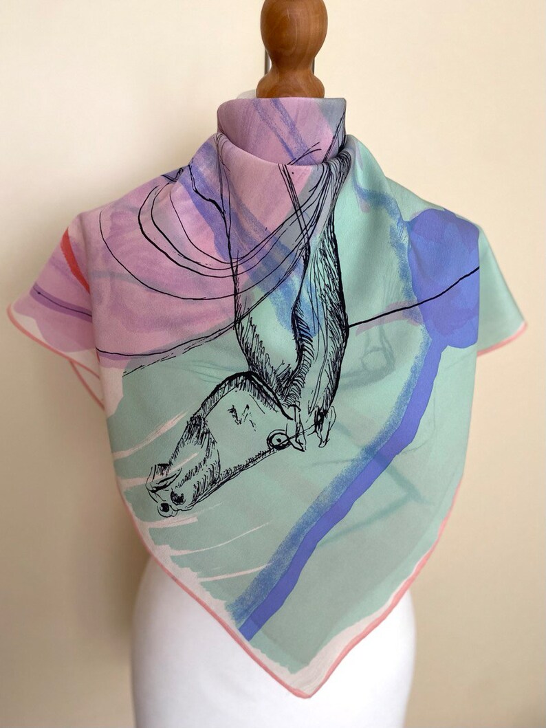 Puede incluir: Un pa&ntilde;uelo de seda cuadrado con un dise&ntilde;o abstracto en rosa, verde y azul. El pa&ntilde;uelo presenta un dibujo en blanco y negro de un p&aacute;jaro en vuelo.