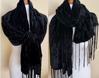 May include: A black velvet scarf with a fringed edge is displayed on a mannequin. The scarf is a rich black and has a soft, textured look. The fringe hangs from the bottom edge of the scarf.