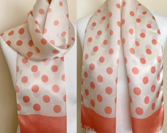 Peut inclure: Un foulard en soie blanc à pois roses. Le foulard a une bordure frangée et est plié en deux.