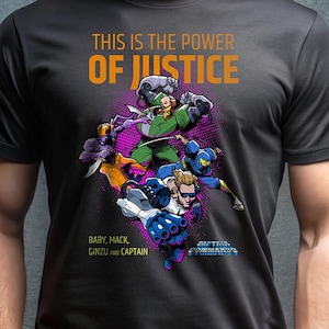 Op de afbeelding: Donkergrijs T-shirt met een kleurrijke afbeelding van stripfiguren. De tekst "THIS IS THE POWER OF JUSTICE" staat boven de personages, met de namen van de personages eronder. Het shirt is gemaakt van een zacht materiaal.