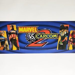 May include: A blue and yellow arcade cabinet marquee with the text "MARVEL VS. CAPCOM 2: New Age of Heroes" and images of characters from the game.
