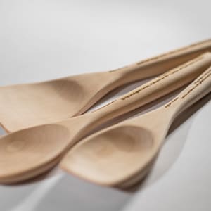 May include: Three wooden spoons, one with a rounded bowl and two with flat, wide bowls. The spoons are made of light wood and have a natural finish. The handles are engraved with text.