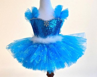 May include: A blue tulle tutu with snowflake print and a sequined bodice. The tutu has a white feather trim and a matching blue snowflake headband.