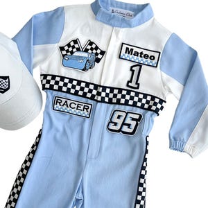 May include: A light blue and white racing-themed jumpsuit with matching white baseball cap. The jumpsuit features a checkered flag design, a car graphic, the name "Mateo", and the number "1" and "95". The cap has a checkered flag logo.