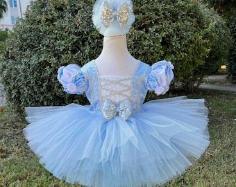 Puede incluir: Un vestido de tul de color azul claro con un corpiño de encaje blanco y una diadema a juego con un lazo azul claro. El vestido tiene una falda de tul con capas y es perfecto para una ocasión especial.