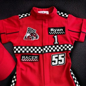 Puede incluir: Mono de carreras rojo con ribetes de cuadros negros y blancos. El mono tiene parches con el nombre "Ryan", los n&uacute;meros "1" y "55", y la palabra "RACER".