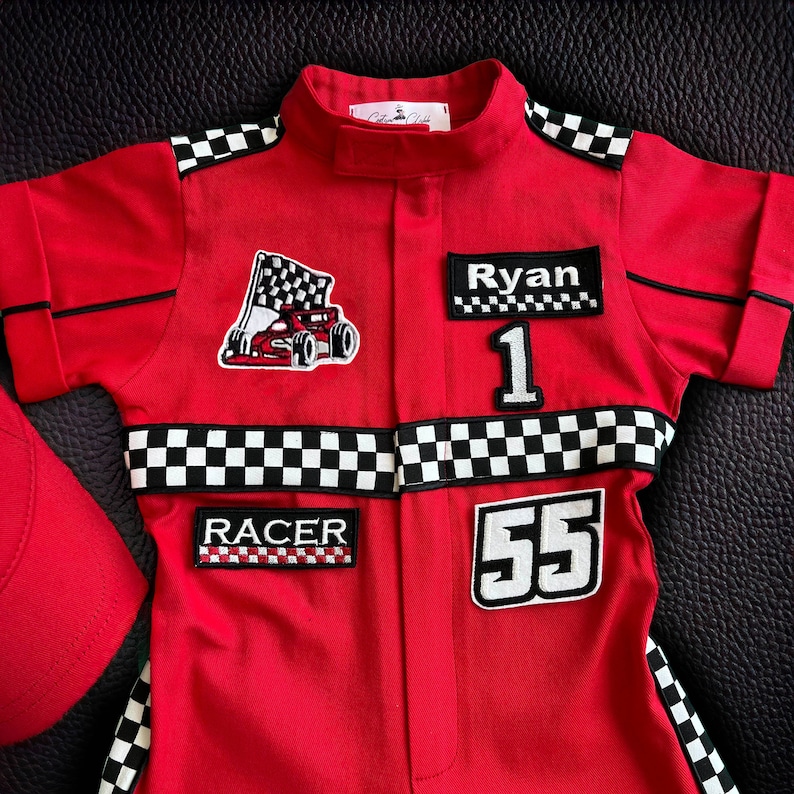 Puede incluir: Mono de carreras rojo con ribetes de cuadros negros y blancos. El mono tiene parches con el nombre "Ryan", los n&uacute;meros "1" y "55", y la palabra "RACER".