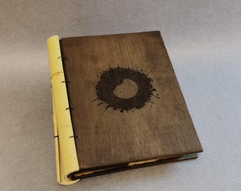 May include: A wooden journal with a bamboo spine. The cover is dark brown with a circular design in the centre. The journal is closed and appears to be new.