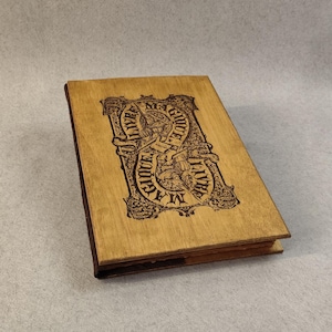 Könnte beinhalten: Ein Holzjournal mit braunem Lederrücken. Der Einband zeigt ein dekoratives Design mit dem Text "In Gloom, I Have Found My Way".