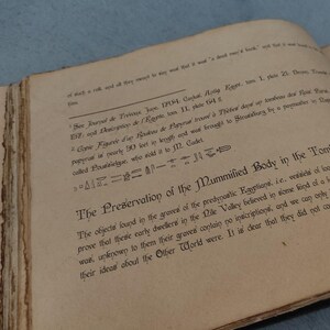 K&ouml;nnte beinhalten: Ein aufgeschlagenes Buch mit gealterten, vergilbten Seiten. Der Text enth&auml;lt den Titel "The Preservation of the Mummified Body in the Tomb" und andere historische Texte. Das Buch scheint ein Antiquit&auml;t zu sein, m&ouml;glicherweise im Zusammenhang mit dem alten &Auml;gypten.