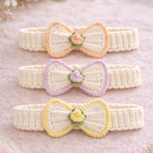 Puede incluir: Tres diademas de ganchillo hechas a mano con lazos. Cada diadema presenta una base color crema con una textura acanalada. Los lazos están delineados en colores pastel: naranja, lavanda y amarillo, cada uno con una pequeña flor en el centro.