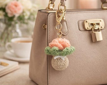 May include: A handmade crochet mushroom keychain in peach, green, and beige hangs from a beige handbag. The mushroom has a peach cap, green gills, and a beige stem. The keychain is attached with a gold-colored clasp.