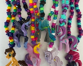 May include: A collection of colorful beaded necklaces featuring plastic pony figurines. The necklaces are made of multi-colored round and star-shaped beads in shades of yellow, blue, green, pink, and purple, each attached to a different pony character.