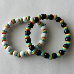May include: Two rainbow friendship bracelets, one with white beads and one with black beads.