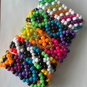 Könnte beinhalten: Ein Stapel bunter Perlenarmbänder, jedes mit einem anderen Muster. Die Armbänder sind aus kleinen, runden Perlen in verschiedenen Farben gefertigt, darunter Grün, Gelb, Orange, Pink, Lila, Blau, Schwarz und Weiß.
