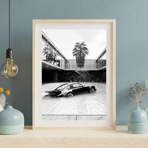 Op de afbeelding: Zwart-wit ingelijste print van een auto in een zwembad. De auto is een klassiek sportwagenontwerp. De scène speelt zich af in een modern architectonisch decor met een palmboom op de achtergrond.
