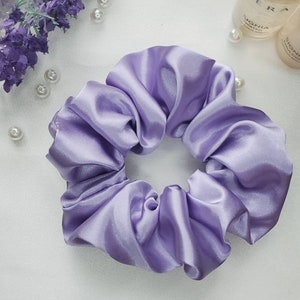 May include: A lavender satin scrunchie for hair. The scrunchie is made of soft, silky fabric and is designed to be gentle on hair.