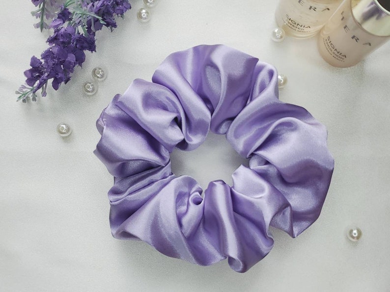 May include: A lavender satin scrunchie for hair. The scrunchie is made of soft, silky fabric and is designed to be gentle on hair.