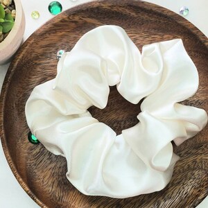 May include: A white satin scrunchie, a hair tie, on a wooden surface.