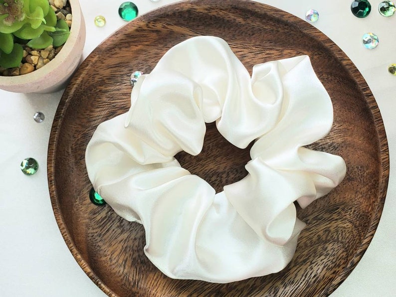 May include: A white satin scrunchie, a hair tie, on a wooden surface.