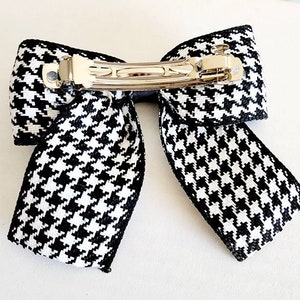 May include: Black and white houndstooth bow hair clip with a silver metal alligator clip.