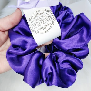 May include: A purple satin scrunchie with a tag that reads "Uniquely Handmade Limited Edition".
