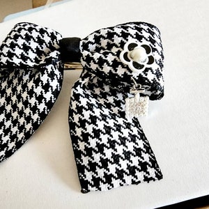 May include: A black and white houndstooth bow with a white flower and a rhinestone charm.