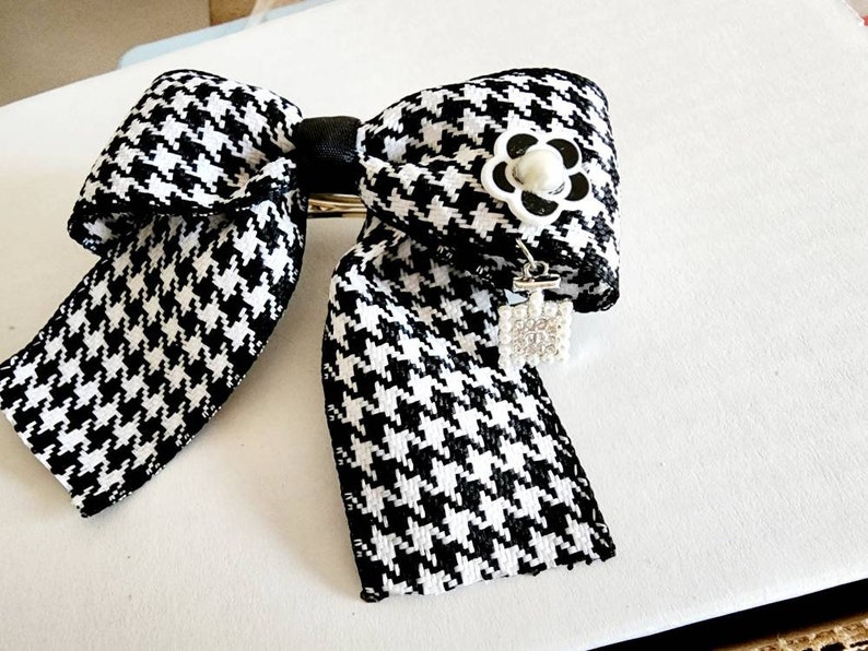 May include: A black and white houndstooth bow with a white flower and a rhinestone charm.