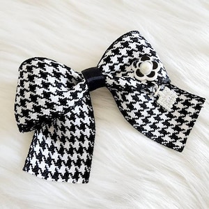 May include: A black and white houndstooth bow with a black ribbon and a white pearl flower accent.