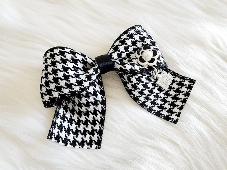 May include: A black and white houndstooth bow with a black ribbon and a white pearl flower accent.