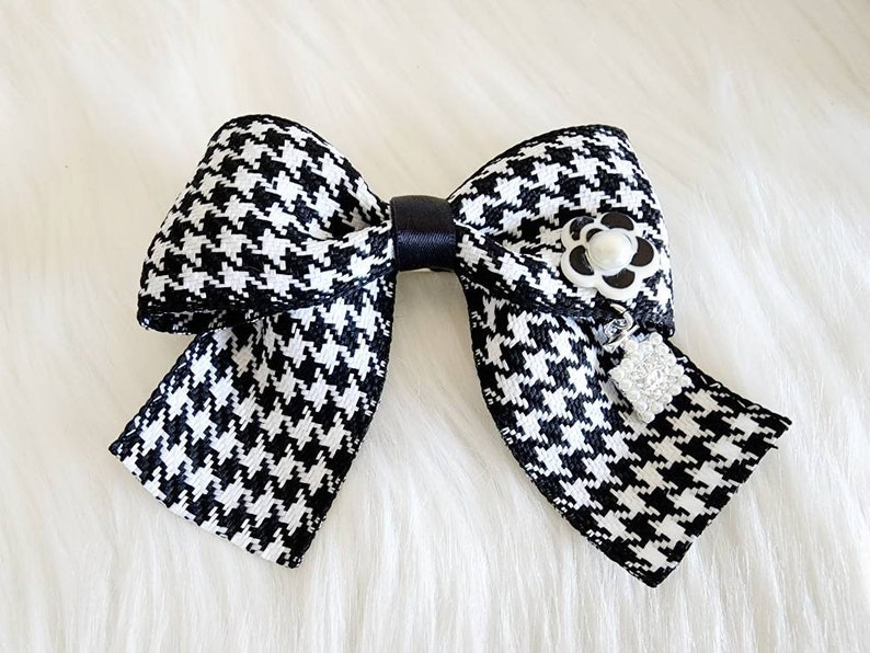 May include: A black and white houndstooth bow with a black satin center and a white pearl flower accent.