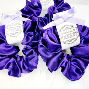 May include: Three purple satin scrunchies with white tags that say "Uniquely Handmade Limited Edition".
