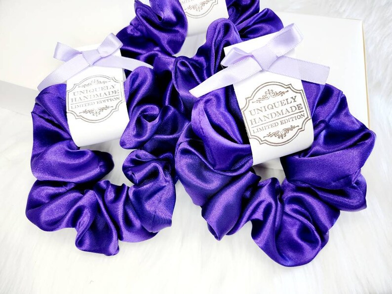 May include: Three purple satin scrunchies with white tags that say "Uniquely Handmade Limited Edition".