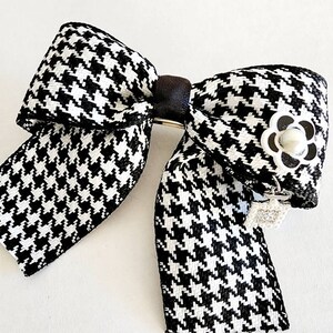 May include: A black and white houndstooth bow with a silver flower accent and a dangling crystal charm.